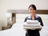Maid working at a hotel holding towels and looking at the camera smiling - housekeeping concepts